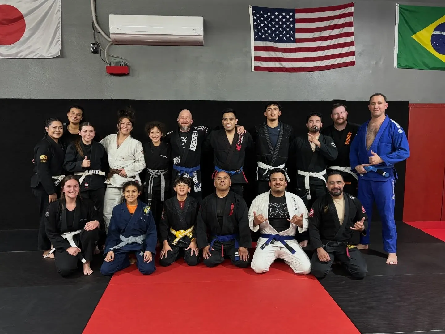 A DNA Jiu Jitsu class in the gi, students and instructors on the mats beneath the academy flags.